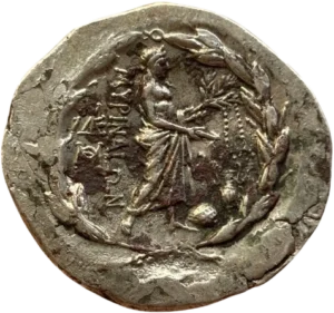 Dans une couronne de lauriers, Apollon à droite, tenant un phiale et une branche de laurier à laquelle sont suspendues deux bandelettes. A ses pieds, l'omphalos et une amphore.