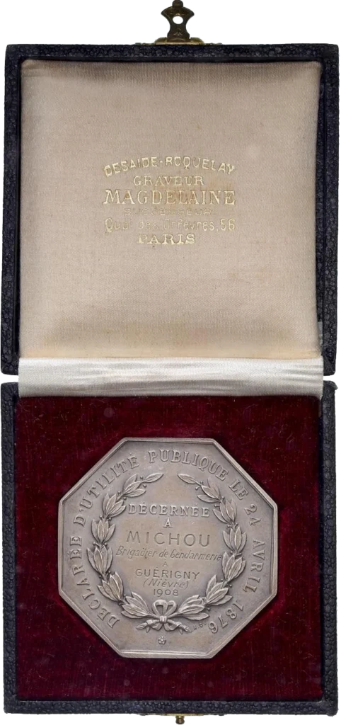 Jeton attribué à Michou, brigadier à Guérigny (Nièvre) en 1908Note : Poinçon corne argent.Jeton vendu dans l'écrin d'origine. Jeton d'aspect vieil argent (mat).