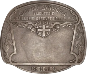 Ecu entouré d'un ruban inscrit "IN SACRA IN QUE CORONAS". sur les cotés des ornements végétaux.