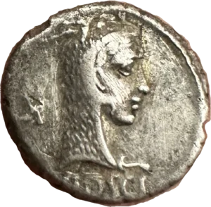 Tête de Junon Sospita à droite, coiffée de la peau de chèvre. derrière le portrait un symbole.